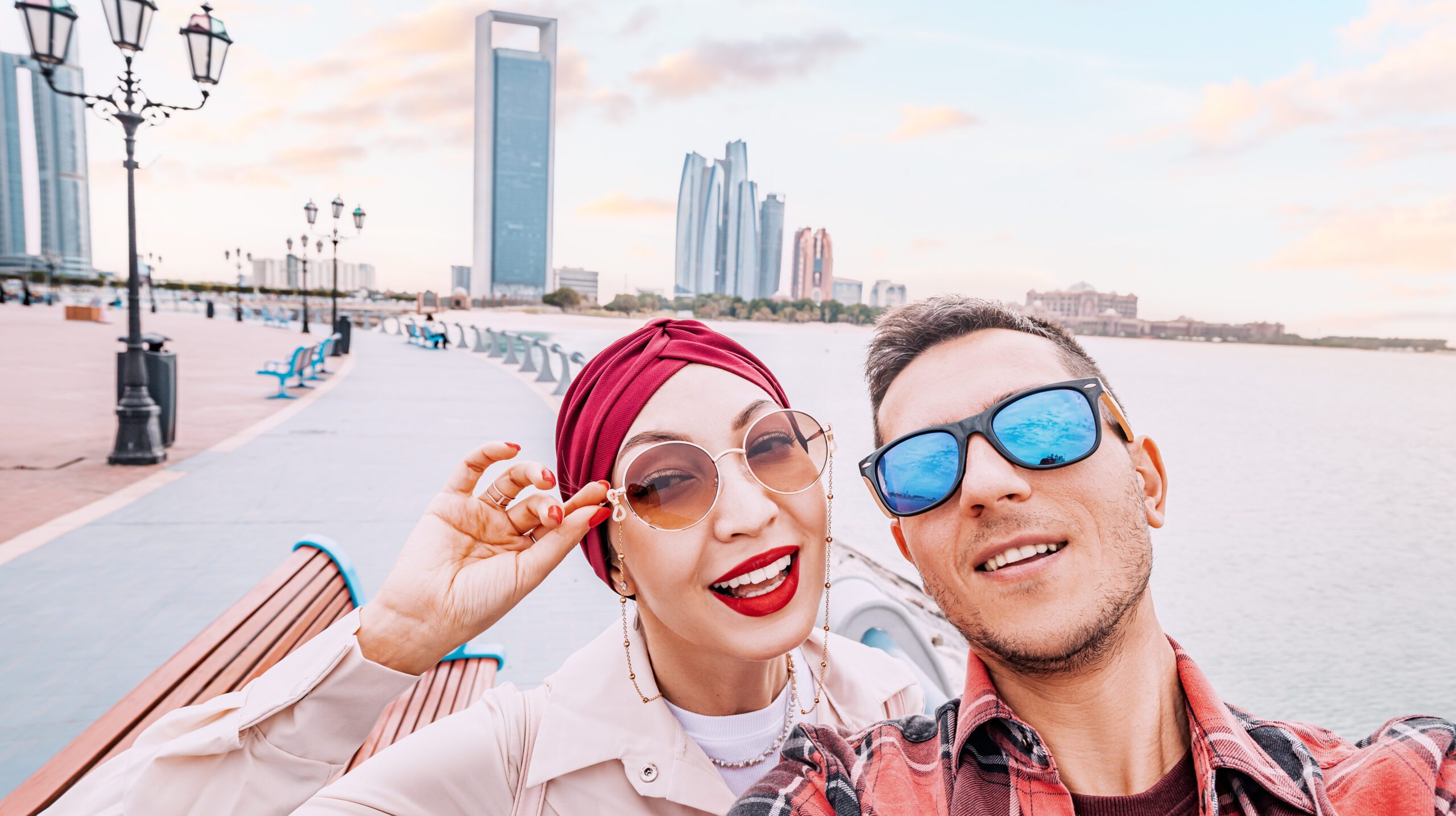Adorable multicultural couple taking selfie photo on Abu Dhabi embankment with scenic view of skyscrapers in downtown