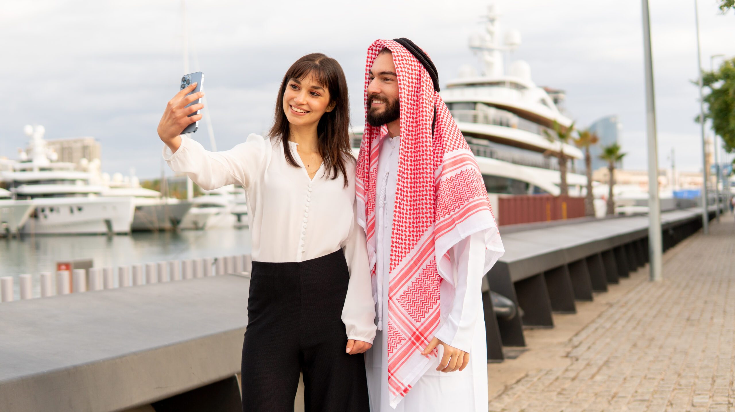 Female manager in formal wear smiling and taking selfie with Arab male client during meeting on embankment