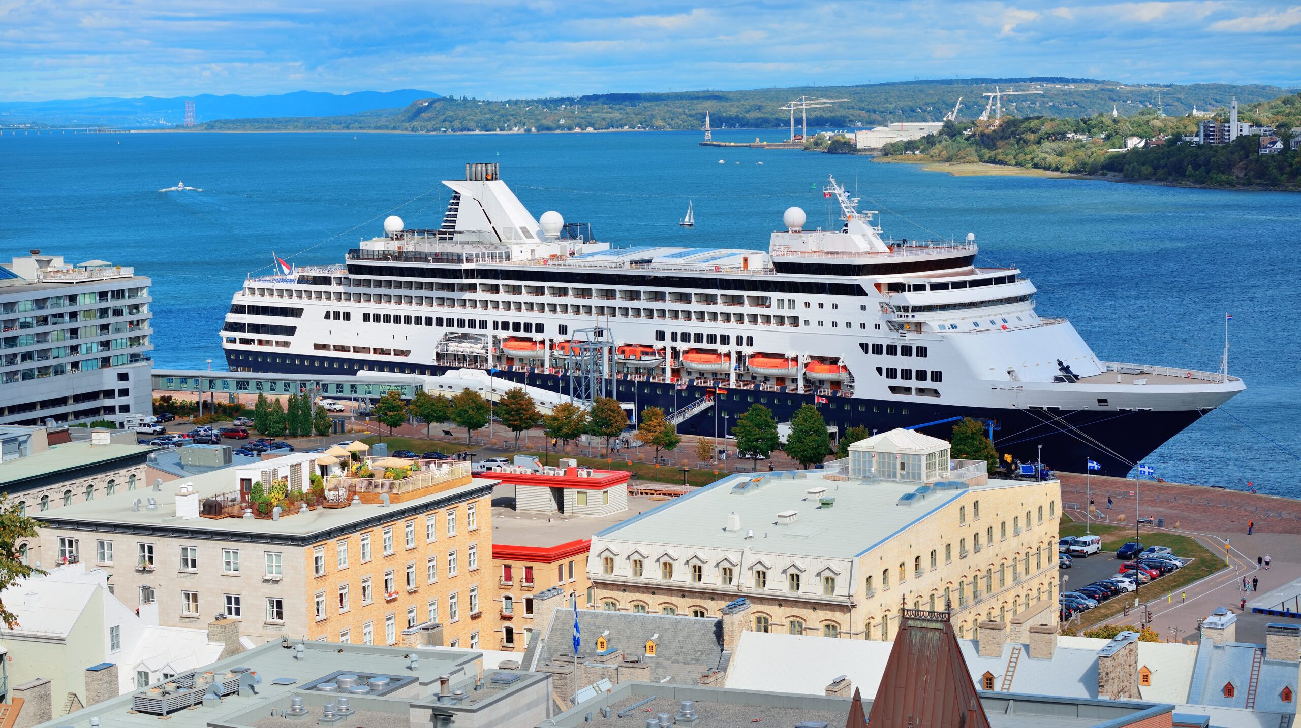 Cruise ship in river in Quebec City with blue sky and historical buildings.