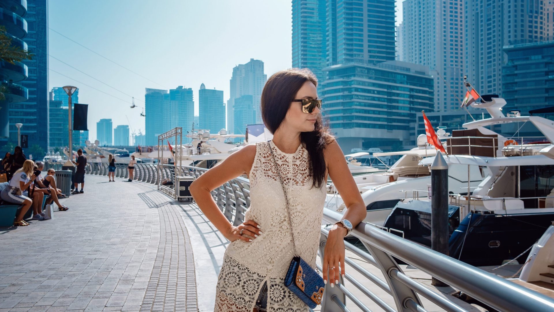 Dubai travel tourist woman on vacation walking on embankment. UAE summer destination. Dubai Marina harbor daylight view. Luxury and comfortable tourism season in UAE. Warm summer day.