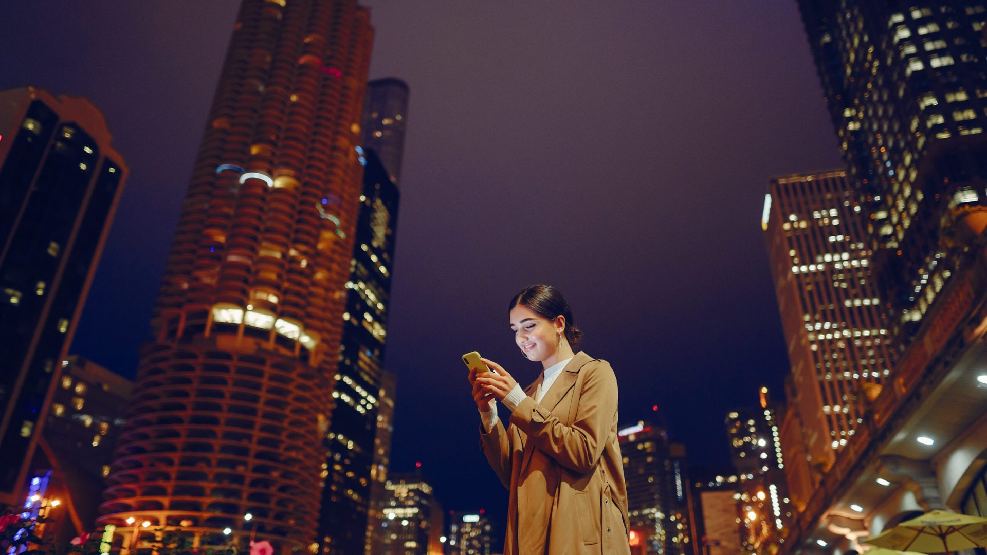 young brunette girl standing at night with phone by Chicago skyline