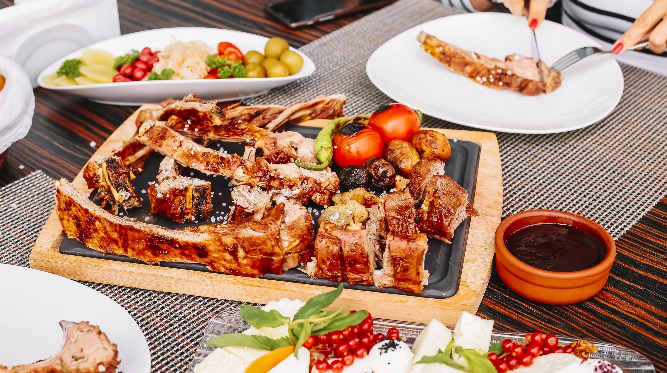 grilled sliced lamb on the wooden board potato tomato pepper pickles side view