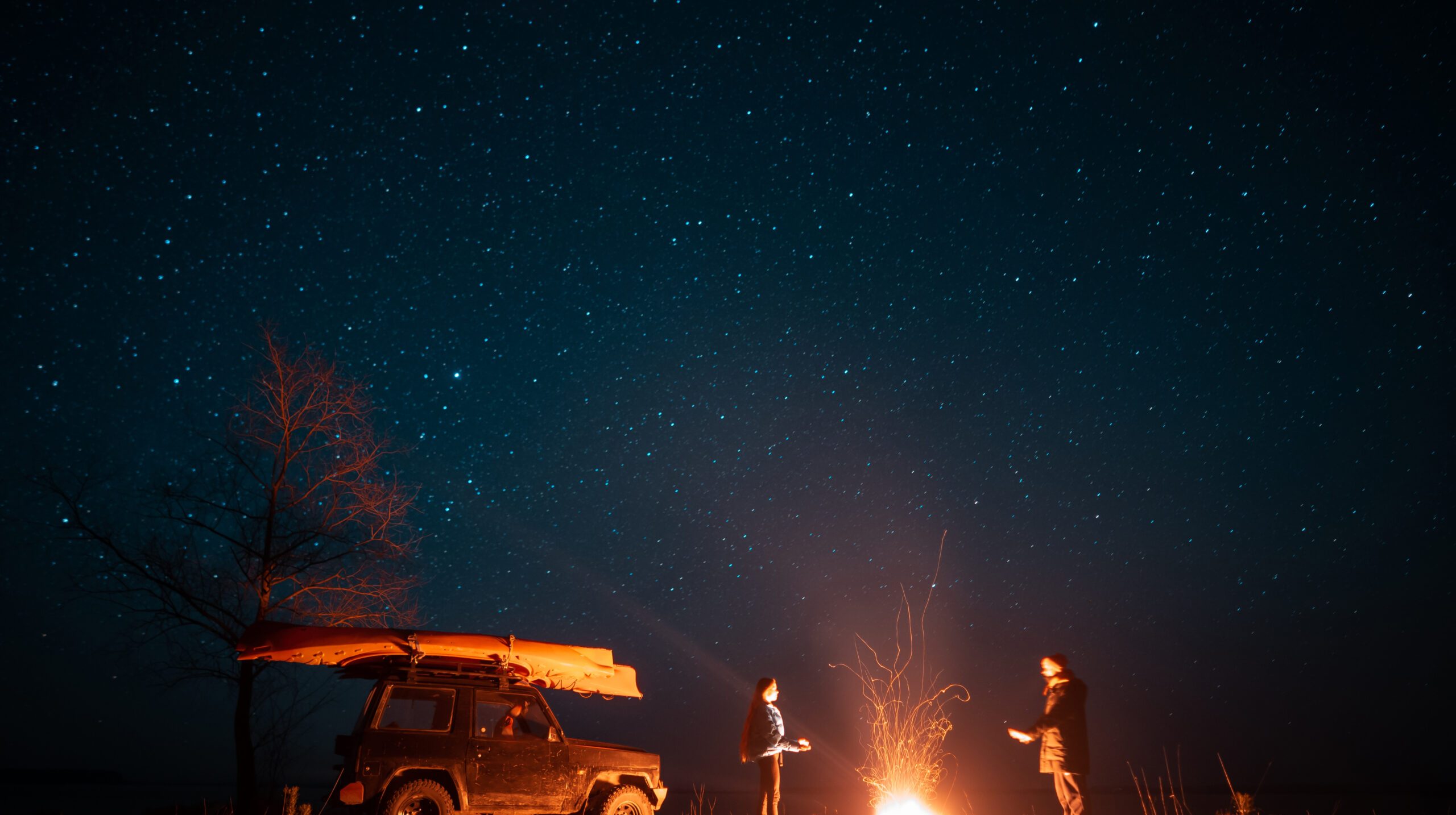 Happy couple man and woman standing in front burning bonfire under starry sky, enjoying quiet night