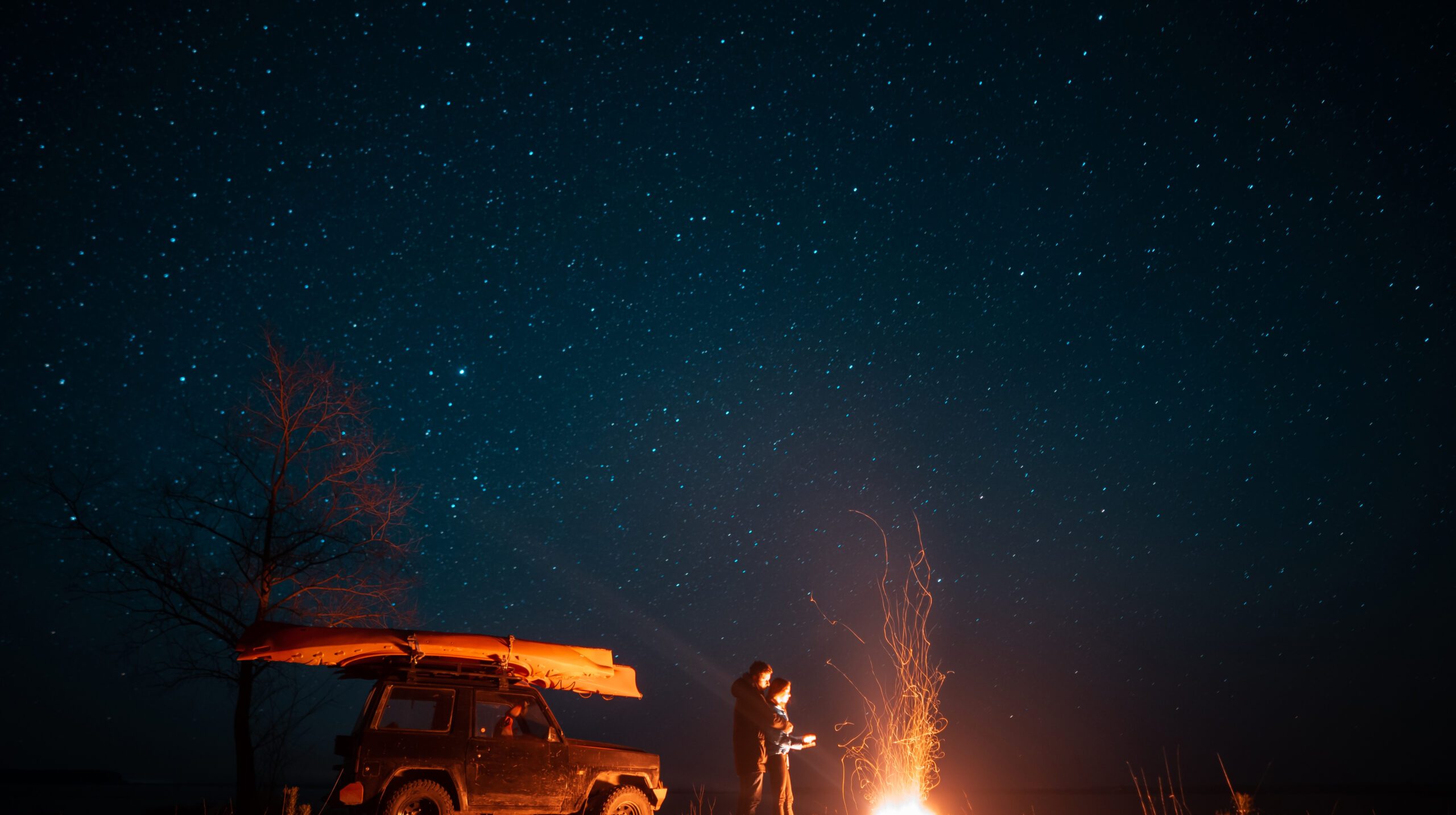 Happy couple man and woman standing in front burning bonfire under starry sky, enjoying quiet night