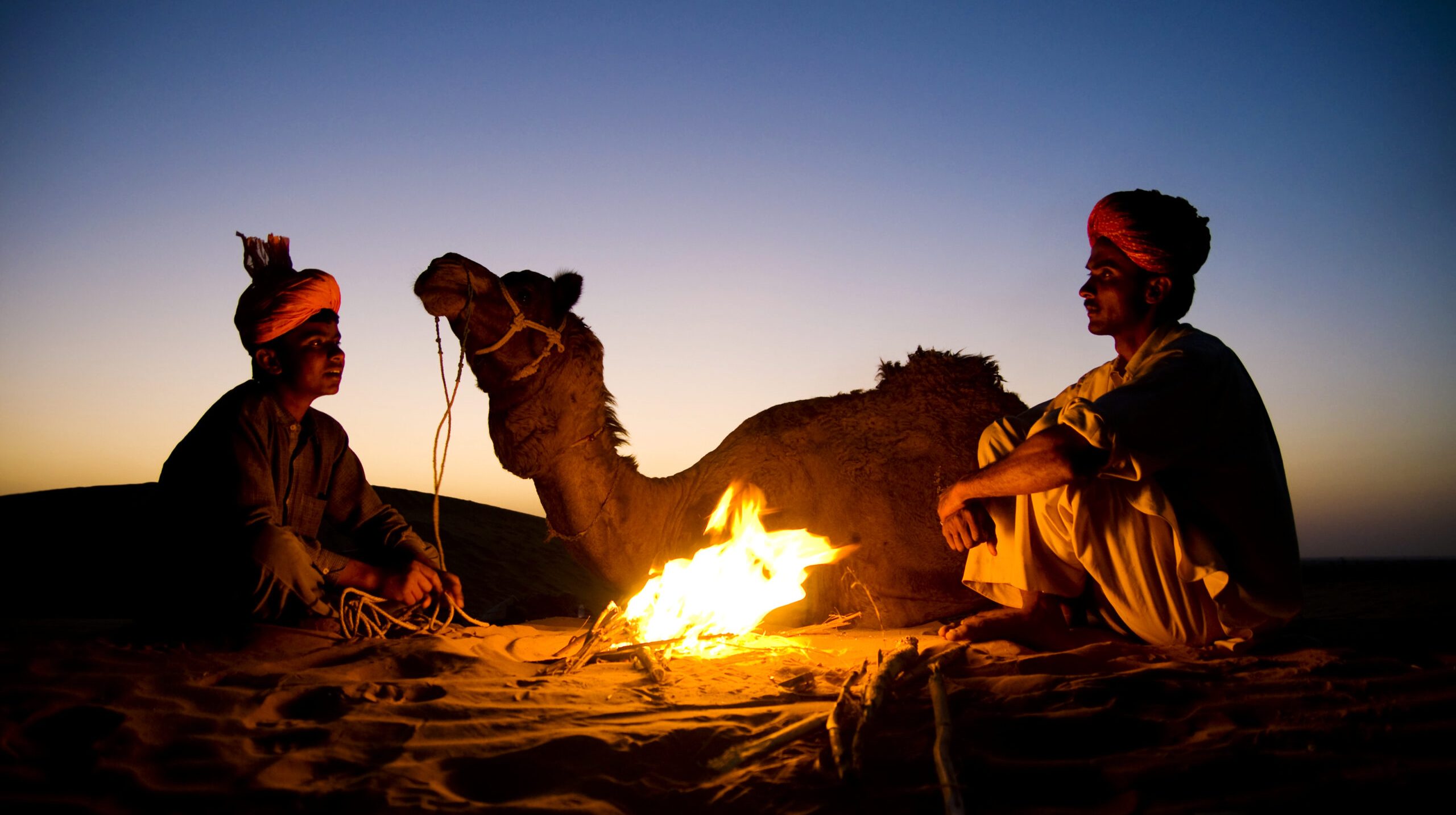 Indian men resting by the bonfire with their camel