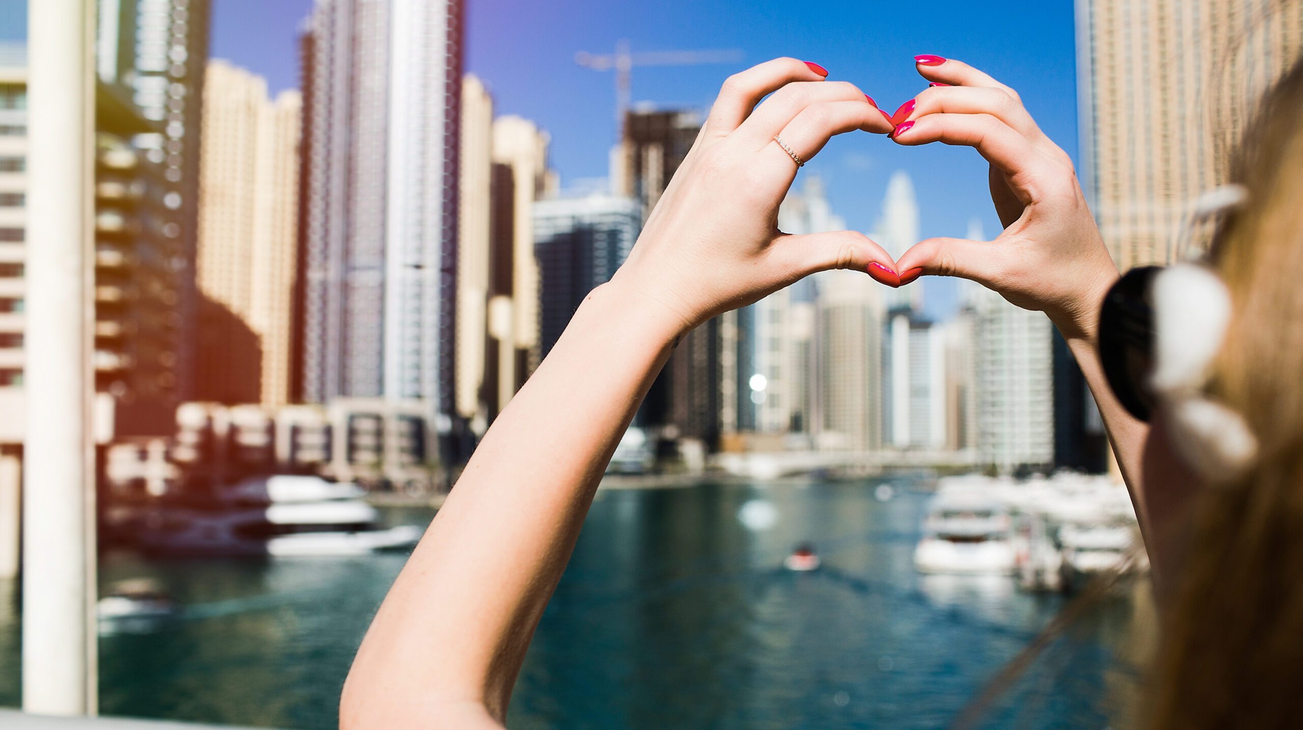Lady with red nails shows heart with her fingers before skyscrapers of Dubai