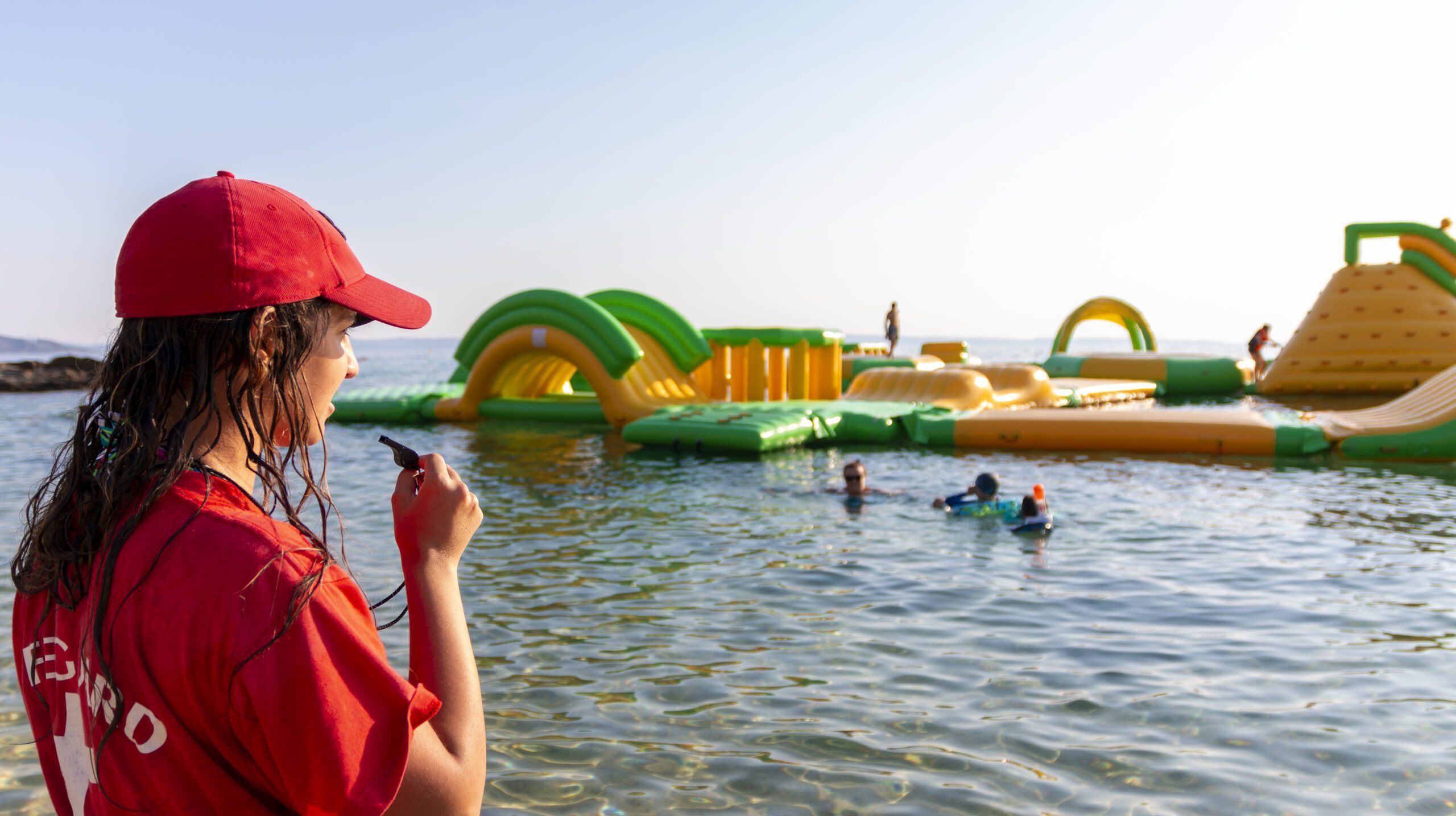 Lifeguard on rescue duty, standing on shore with whistle and looking to the Aquapark. Safety control on vacation. Babysitting on the water
