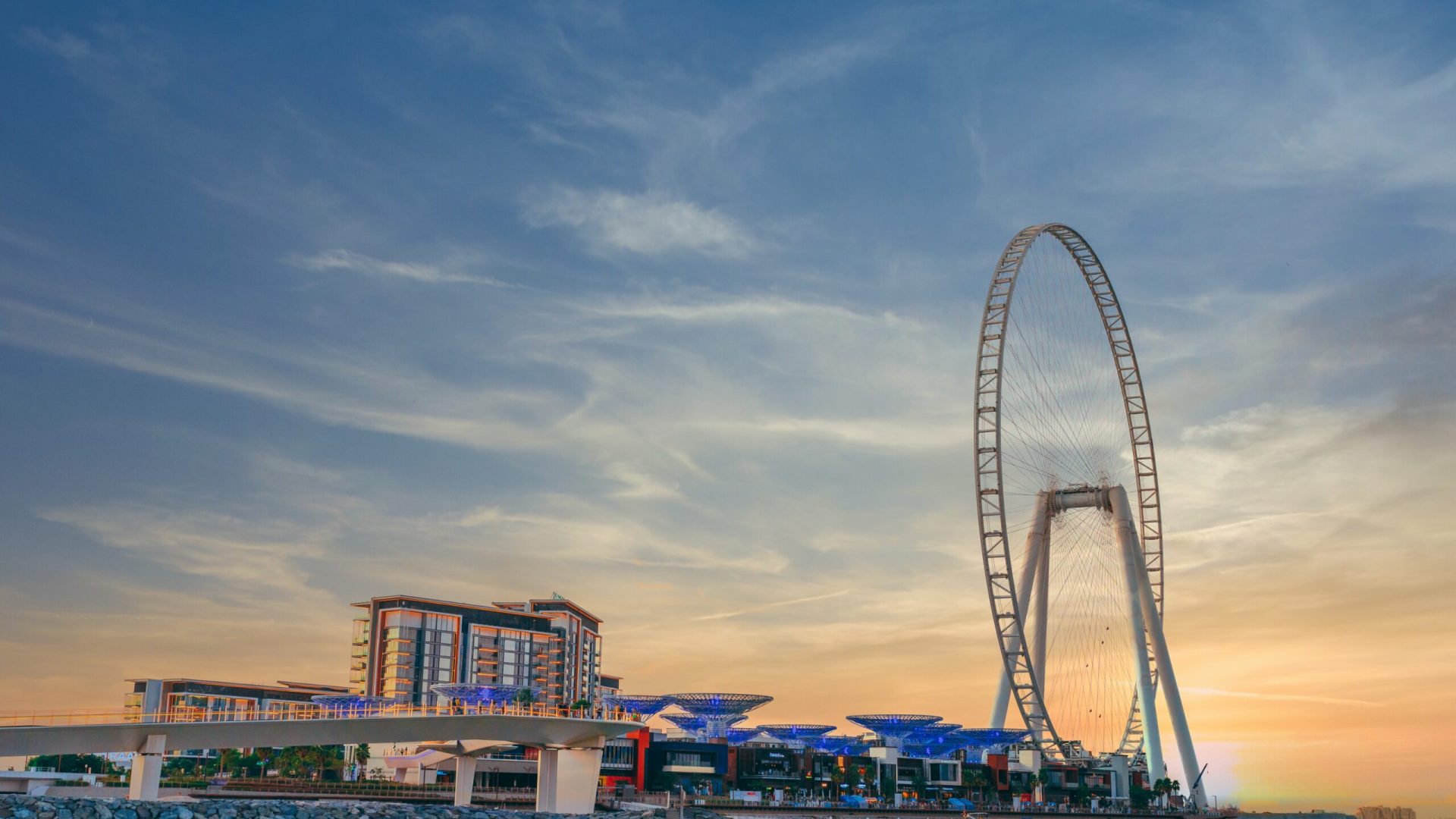 A low angle shot of modern design of a building with a huge Ferris wheel at Bluewaters island in Dubai
