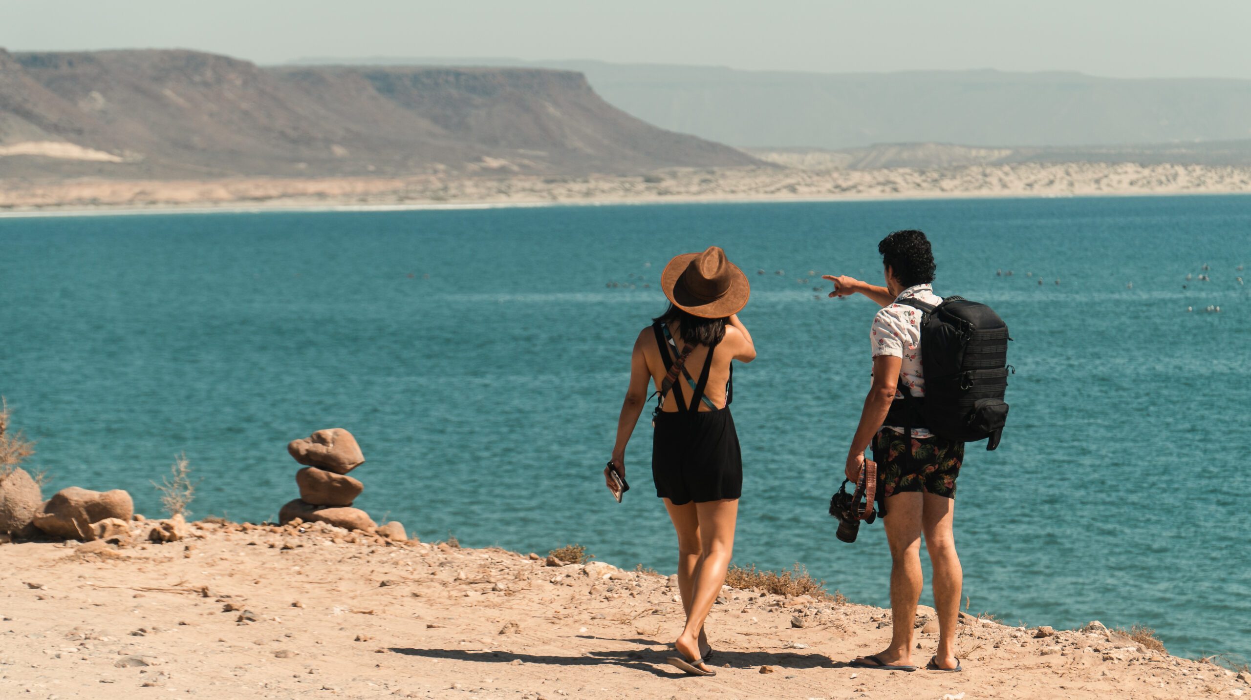 male-female-photographer-couple-stand-cliffside-overlooking-blue-sea-mexico