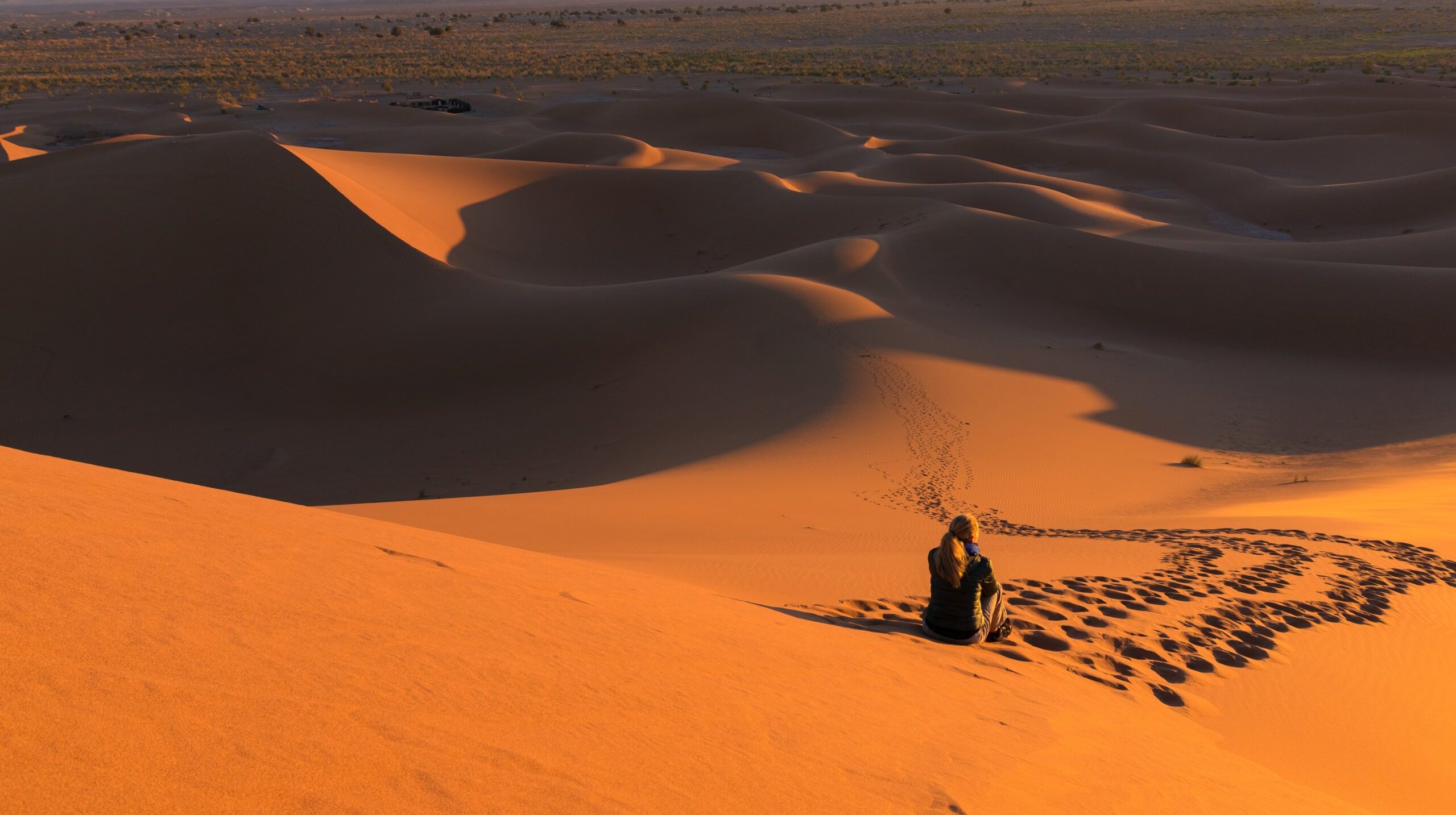 A man sitting on sand dunes surrounded by tracks at a desert