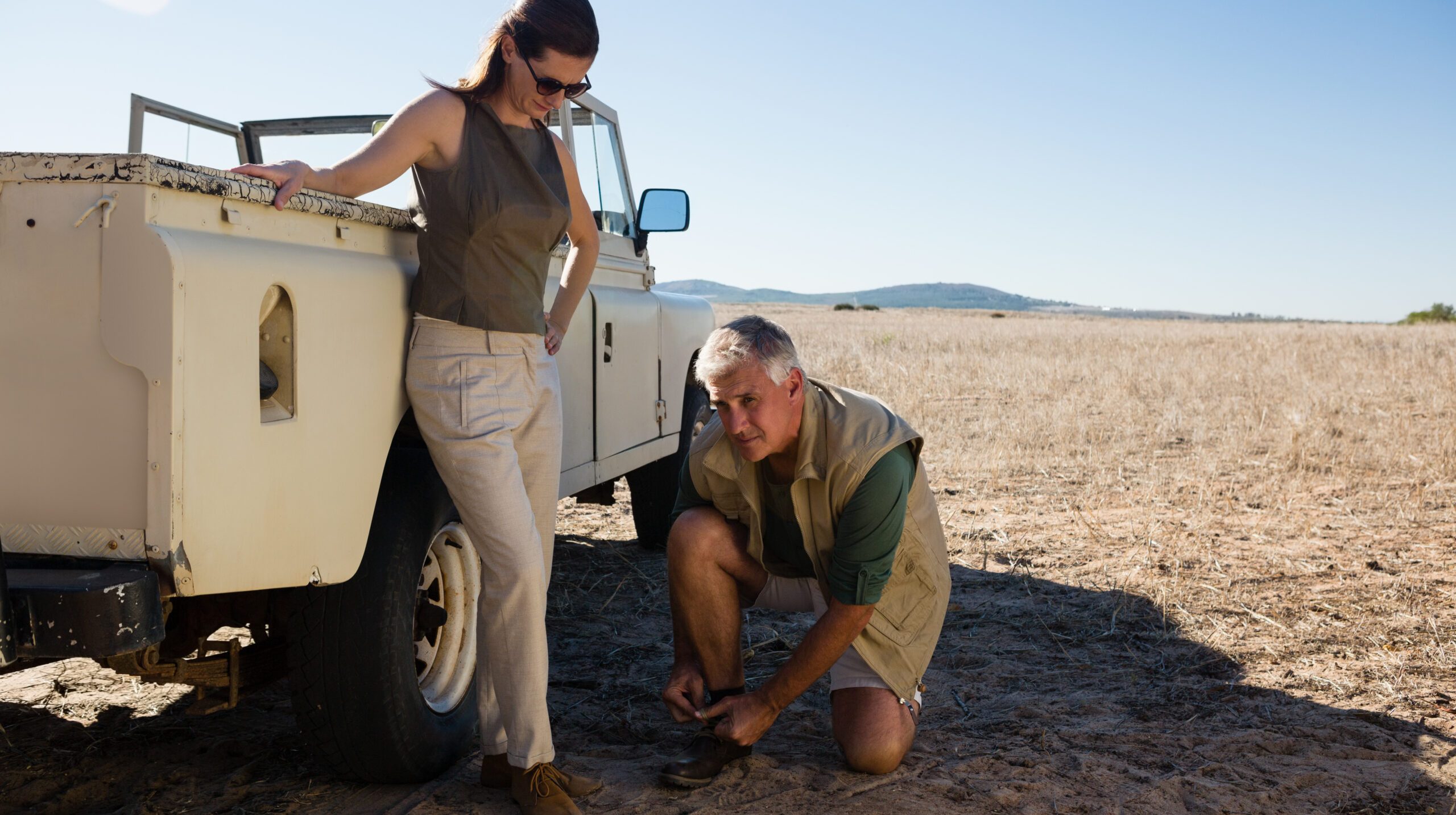 Man with woman tying shoelace by off road vehicle on landscape