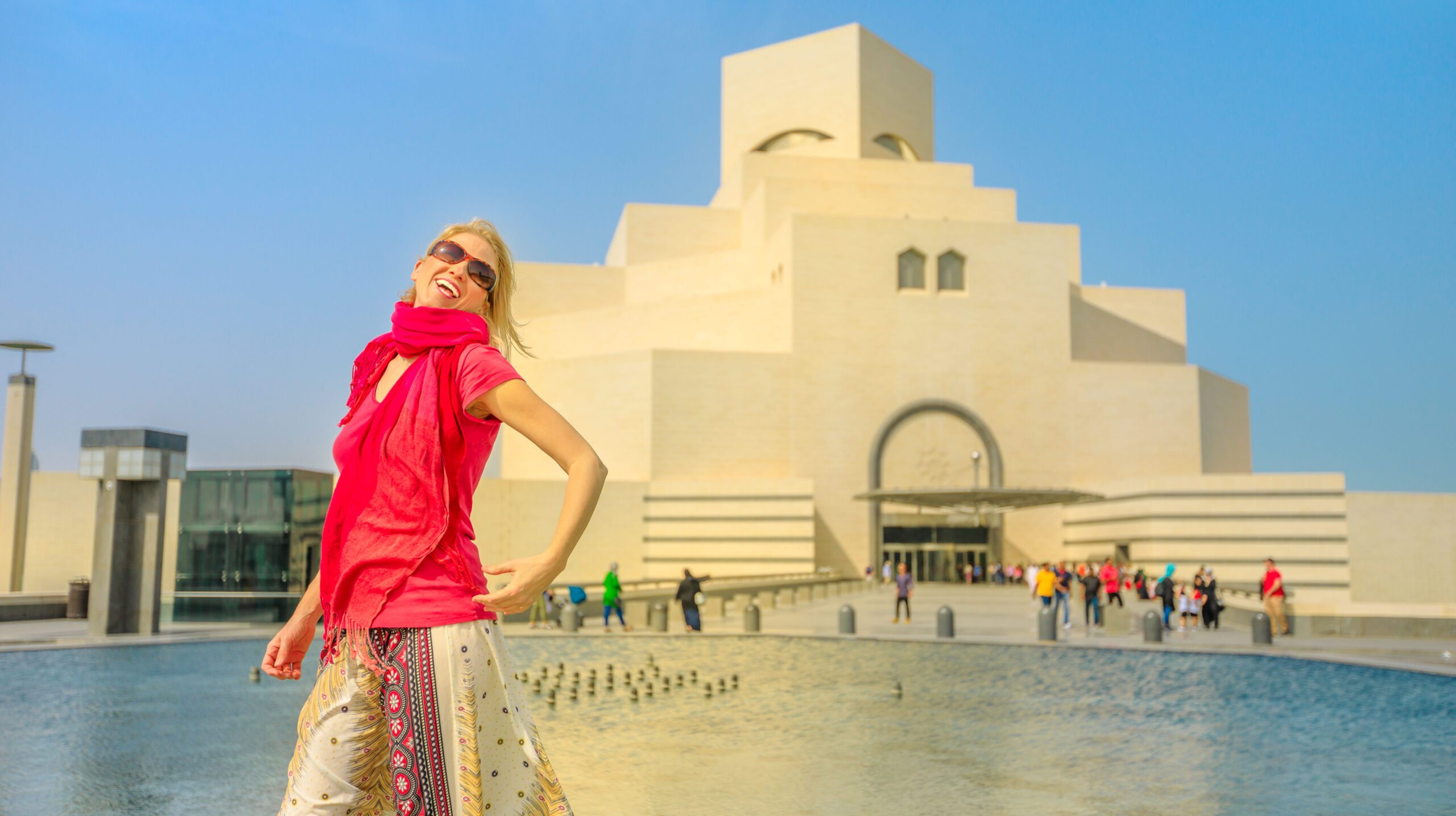 Happy woman in front of famous museum located along the Corniche near Dhow Harbor in Qatari capital. Caucasian tourist enjoying in Doha, Middle East, Arabian Peninsula in Arabian Gulf. Sunny blue sky.