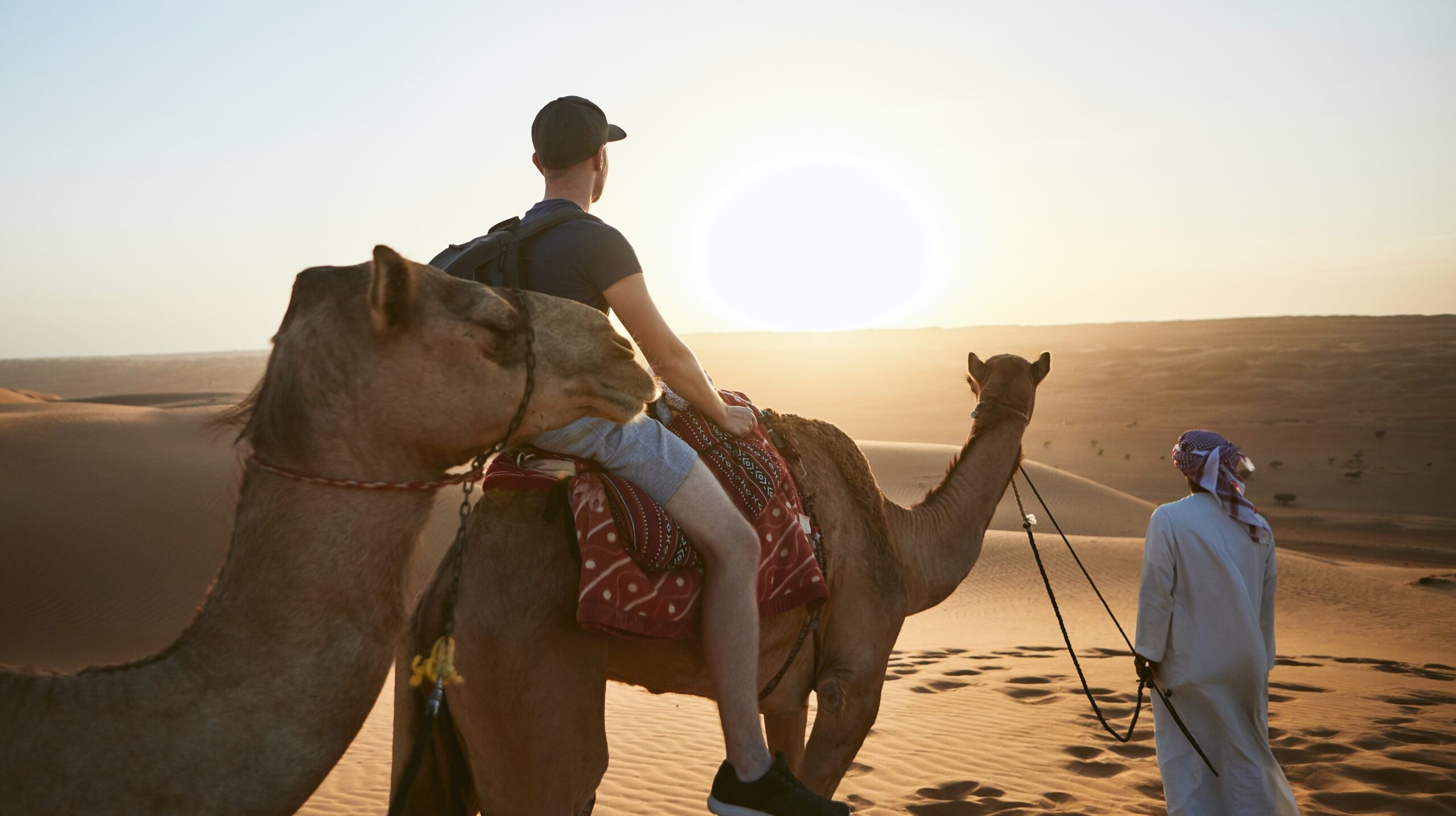 Camel riding in desert at amazing sunset. Young man enjoying journey on sand dunes. Wahiba Sands in Sultanate of Oman