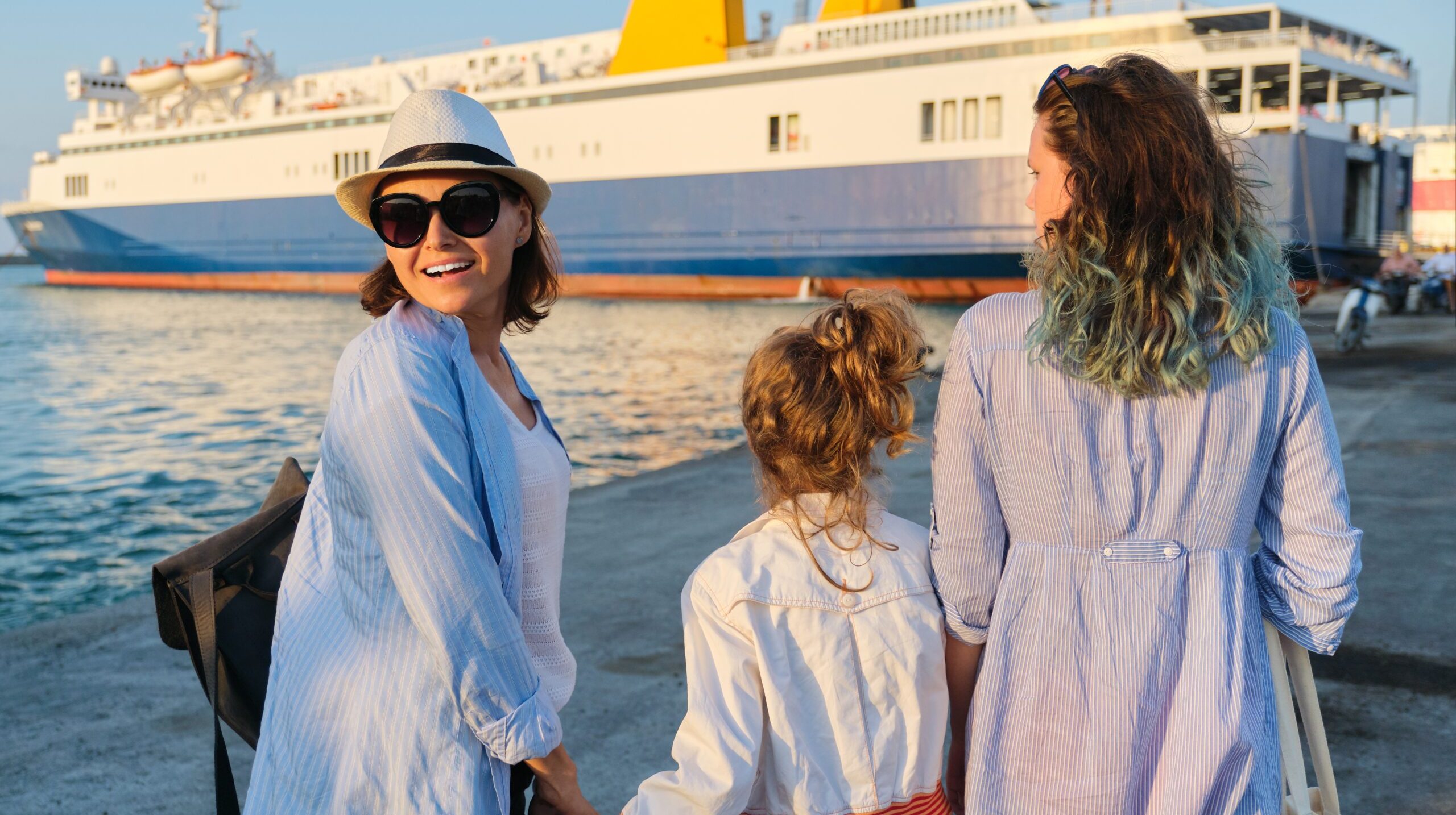 Sea family vacation, mother and daughters in the seaport holding hands looking at the ferry