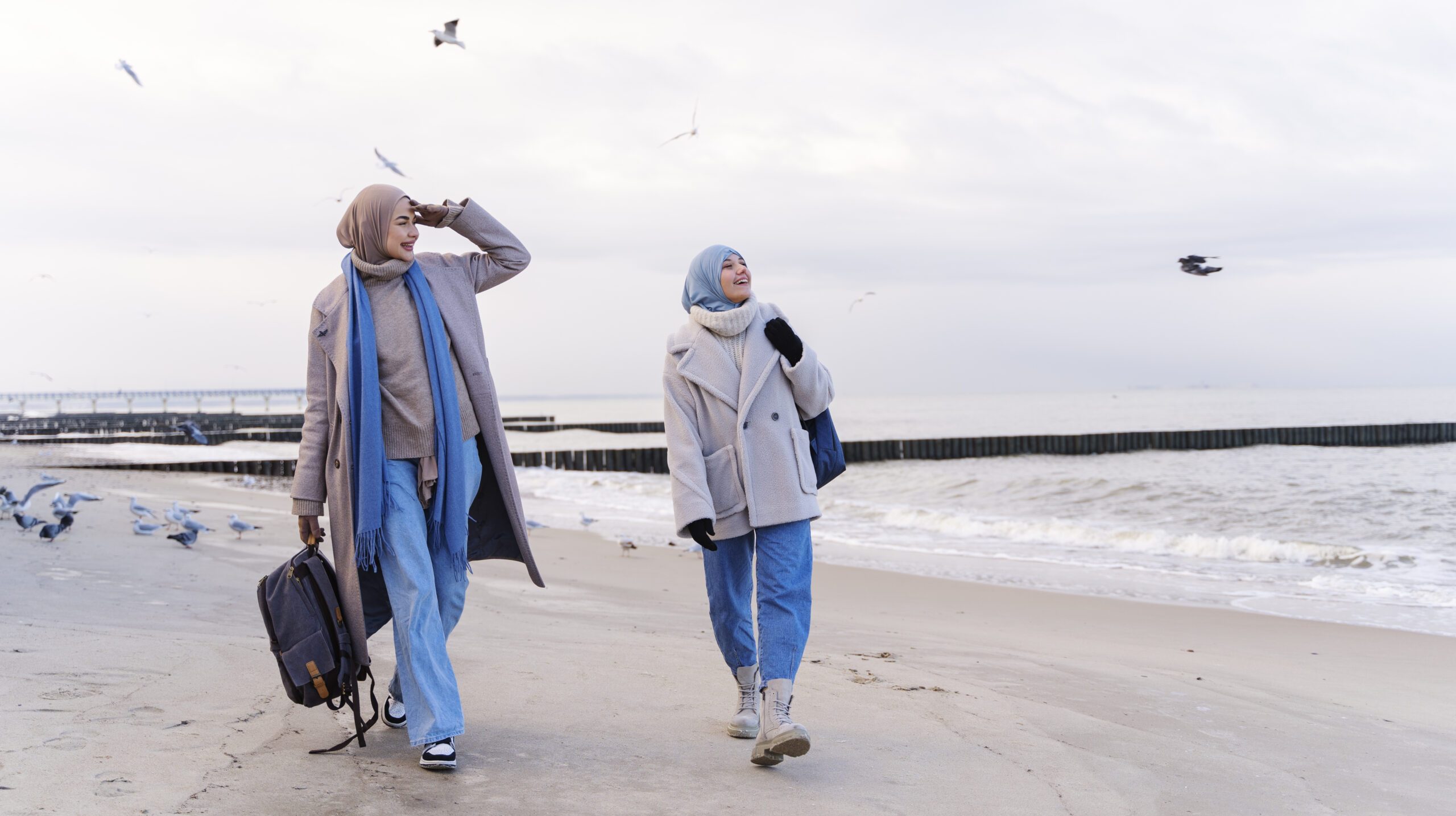 two-muslim-female-friends-walking-by-beach-while-traveling