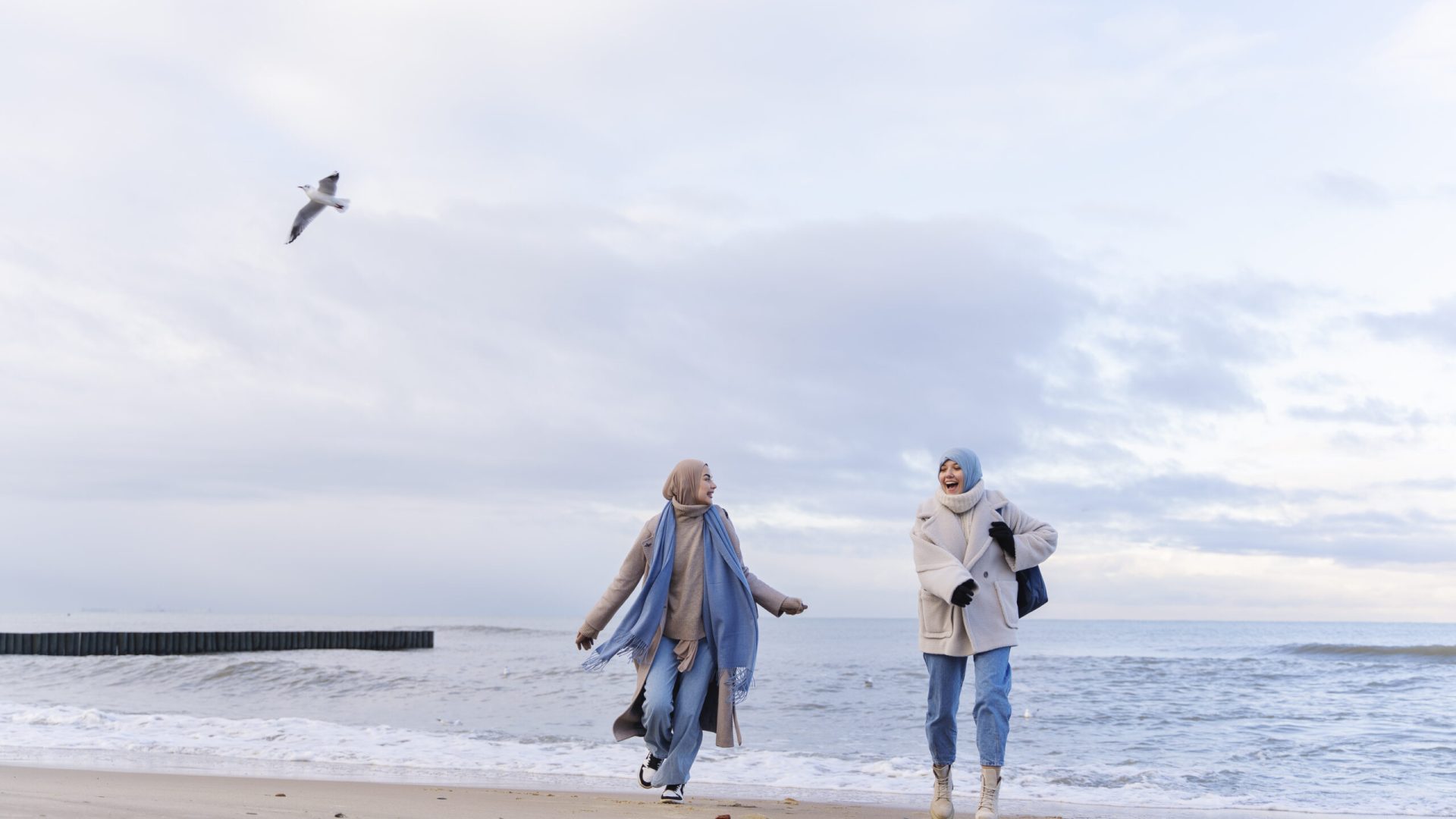 two-muslim-female-friends-walking-by-beach-while-traveling
