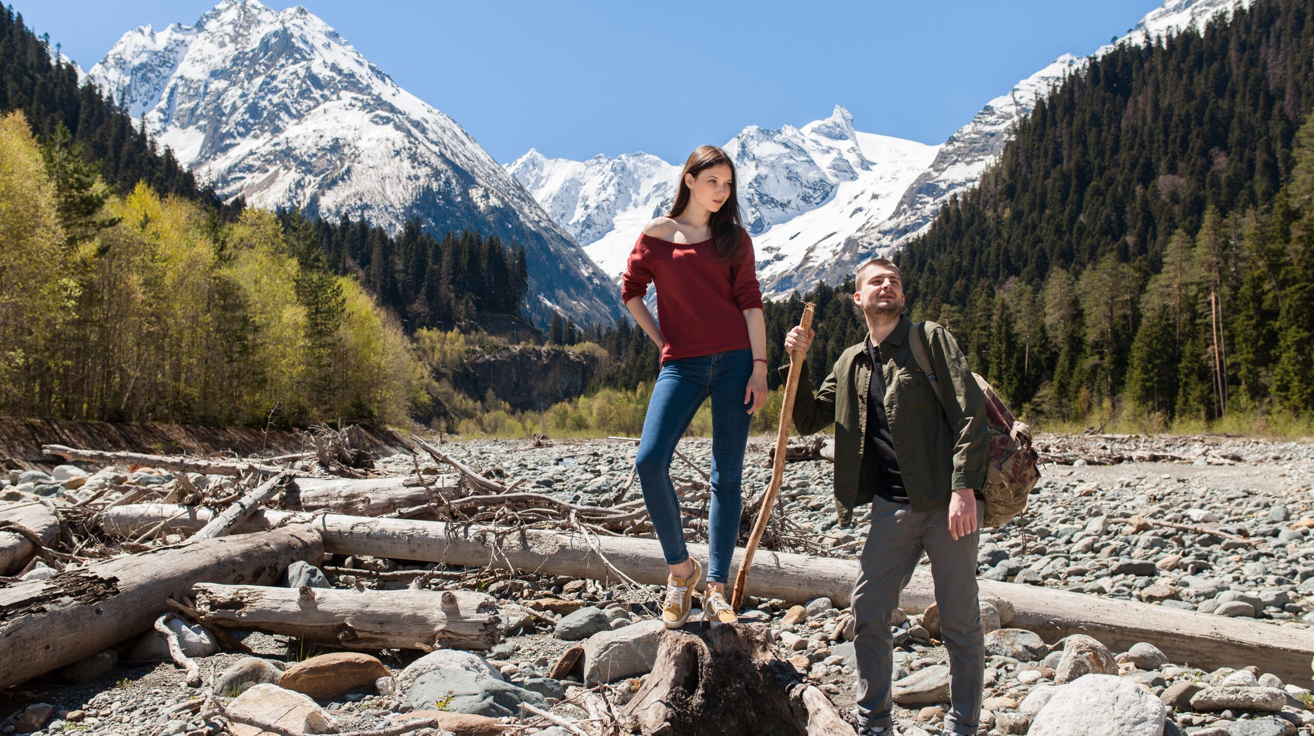 young hipster beautiful couple hiking at river in forest, jeans, sneakers, smiling, having fun, traveling, romantic vacation, mountains background