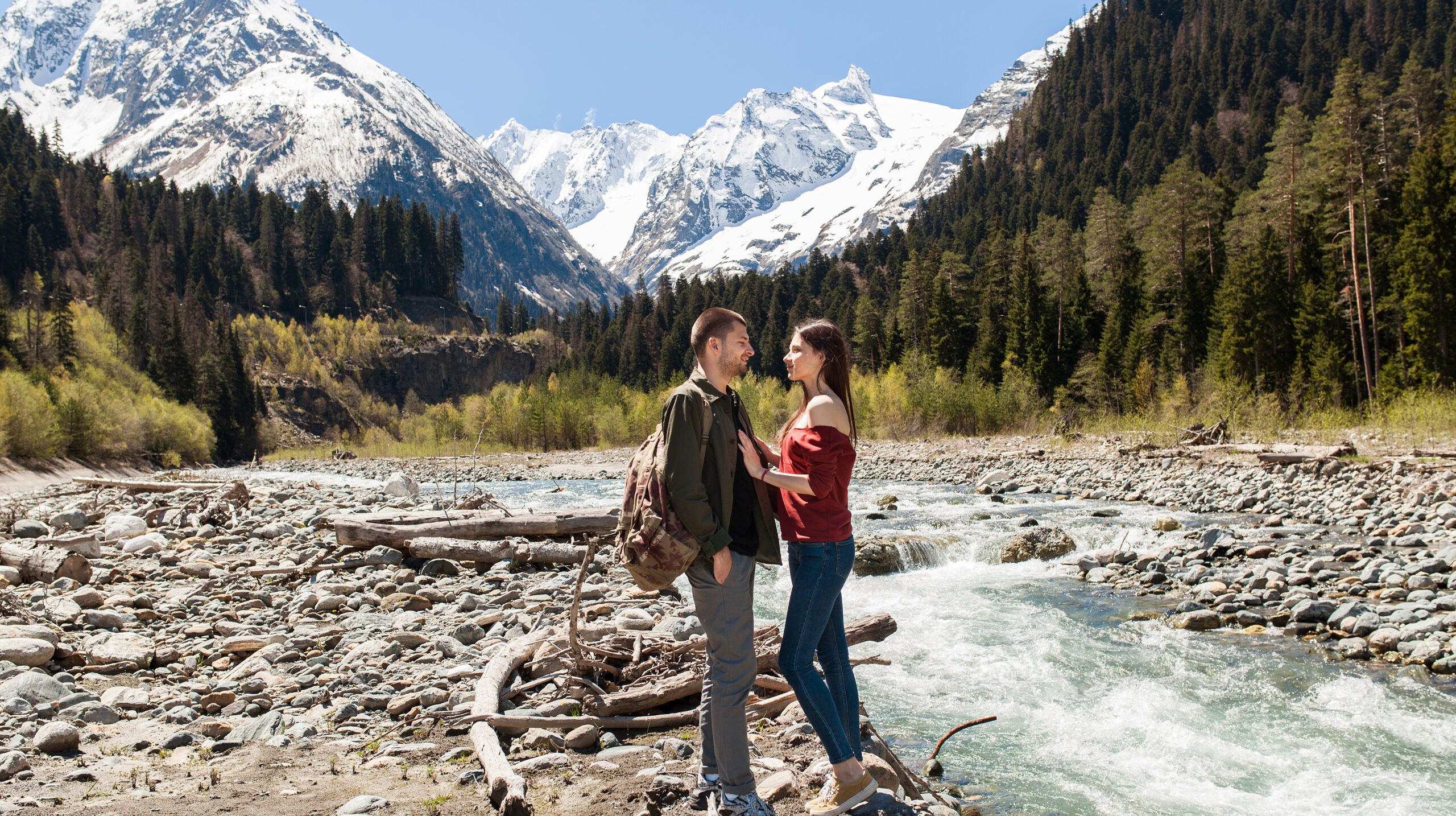 young hipster beautiful couple hiking at river in forest, jeans, sneakers, smiling, having fun, traveling, romantic vacation, mountains background