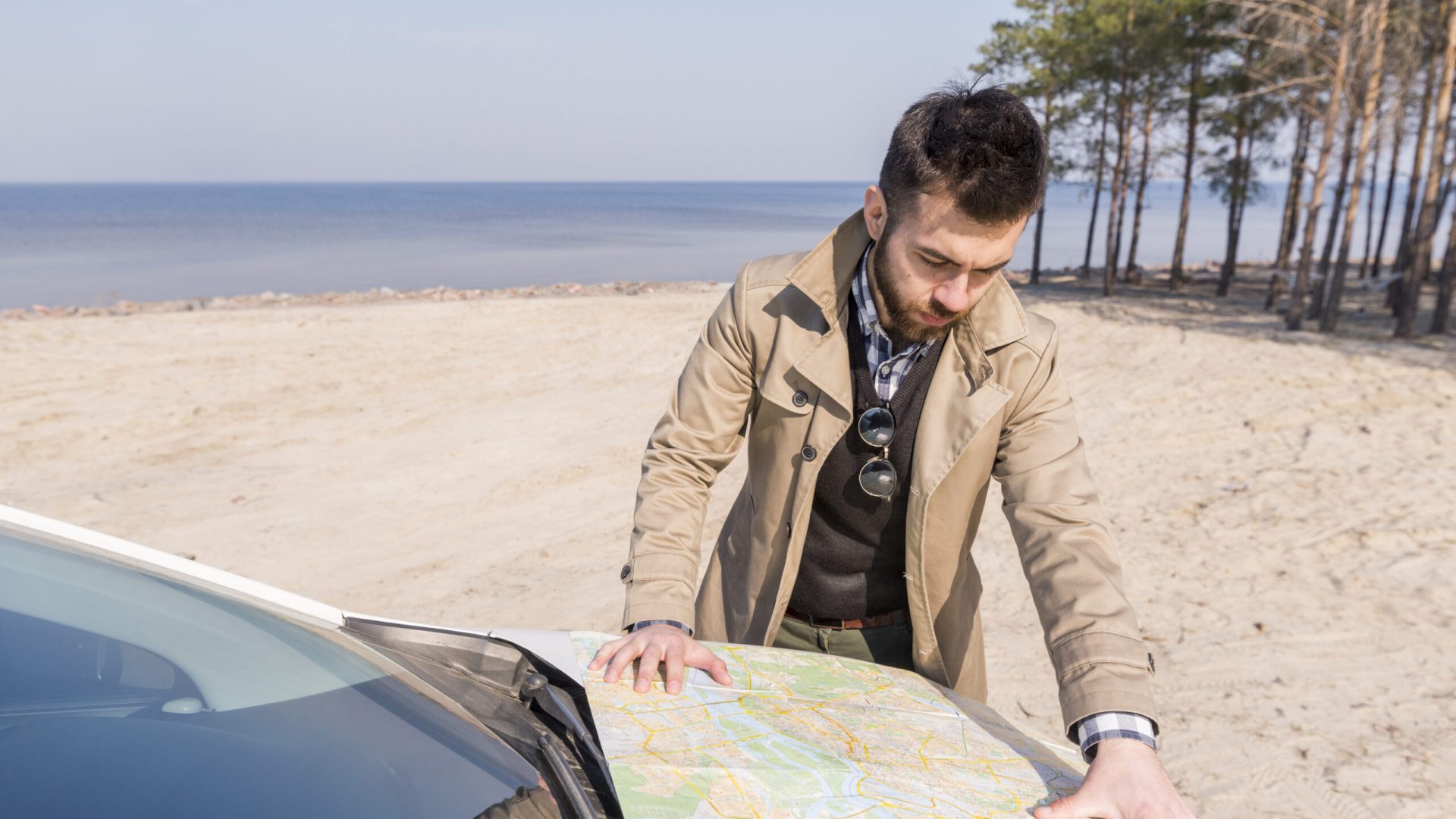 young-male-traveler-searching-location-map-car-bonnet-beach